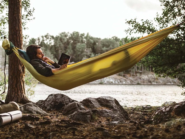 Man enjoying a book while in a hammock next to water