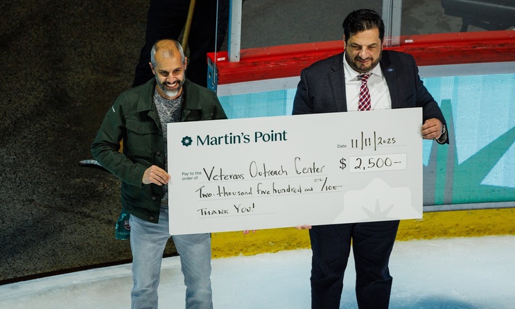 Men holding donation check inside of ice hockey rink