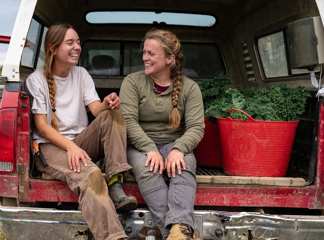 two young women in farm truck with vegetables