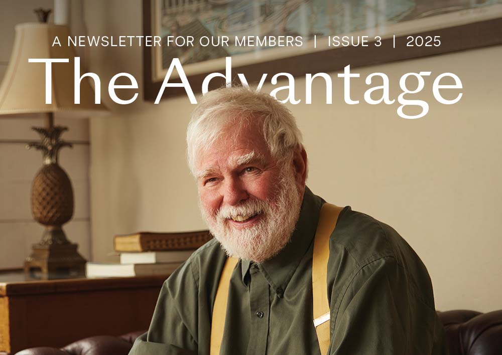 Older man with white hair and beard smiling while seated indoors, featured on the cover of The Advantage Issue 3 (2025).