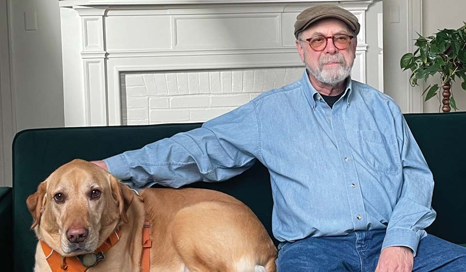 Bud sitting on a dark green couch beside a large tan dog in front of a white fireplace.