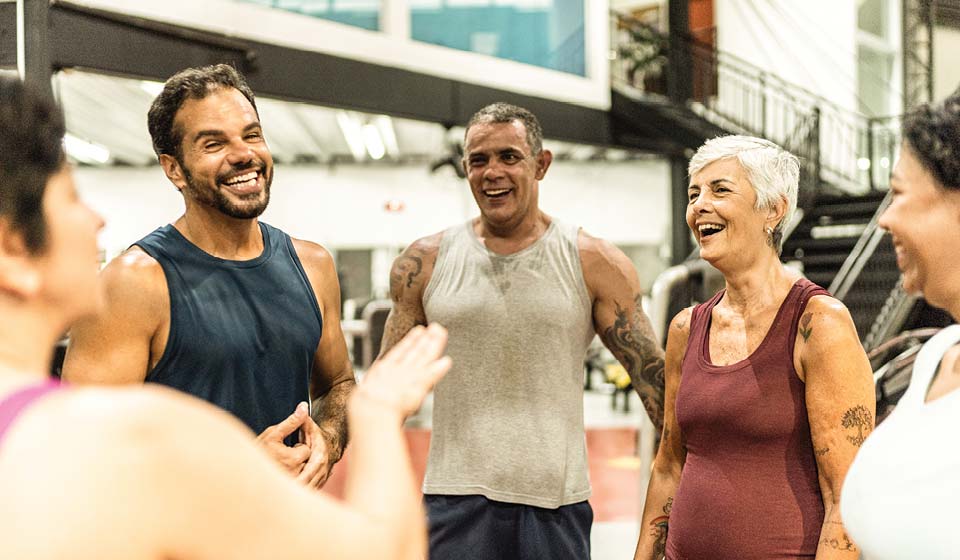 Group of adults laughing together after exercising in a gym.