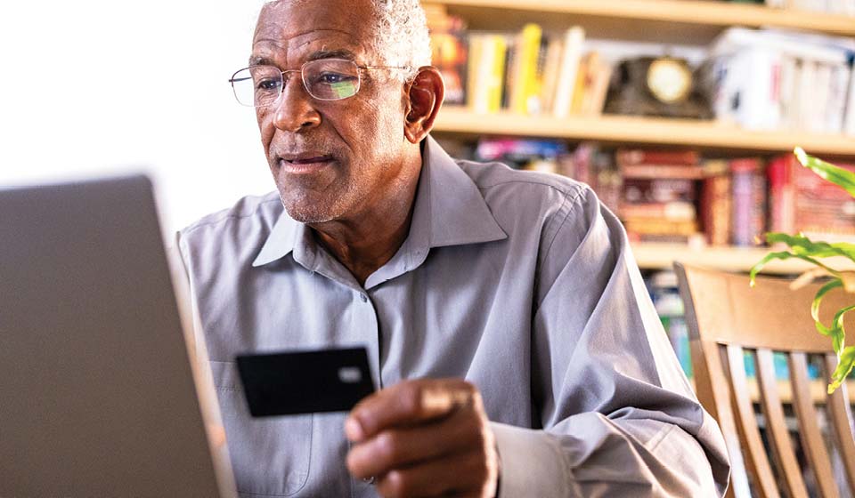 Older man using a laptop while holding a credit card at home.