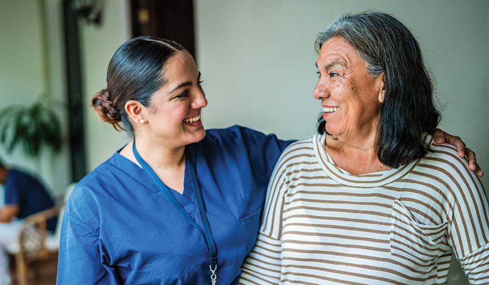 Nurse and older woman smiling and talking together indoors.