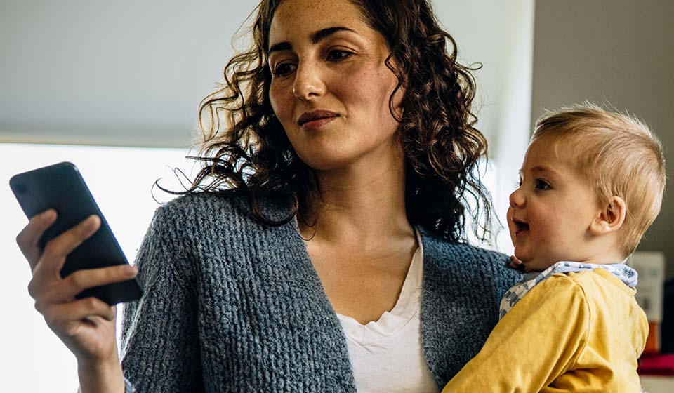 Mother holding her baby while looking at her smartphone.