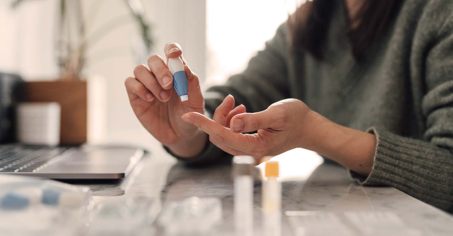 Person using a blood glucose monitor to check blood sugar at home.