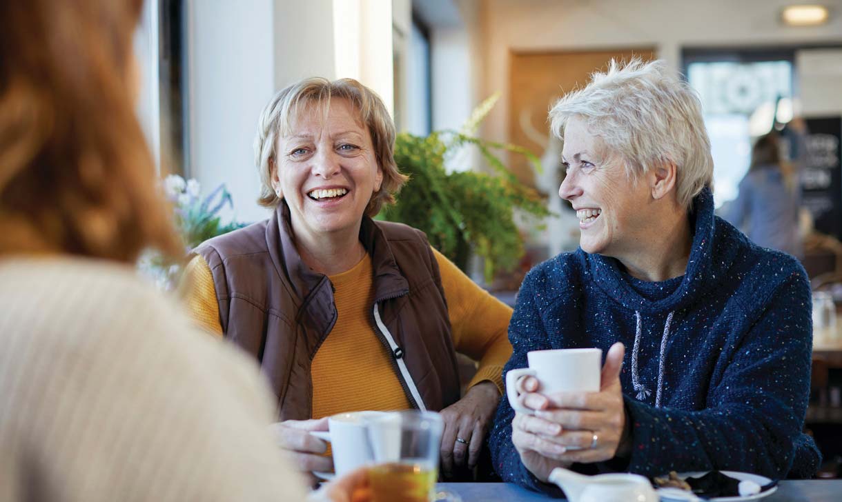 Two senior women laughing together while having coffee.
