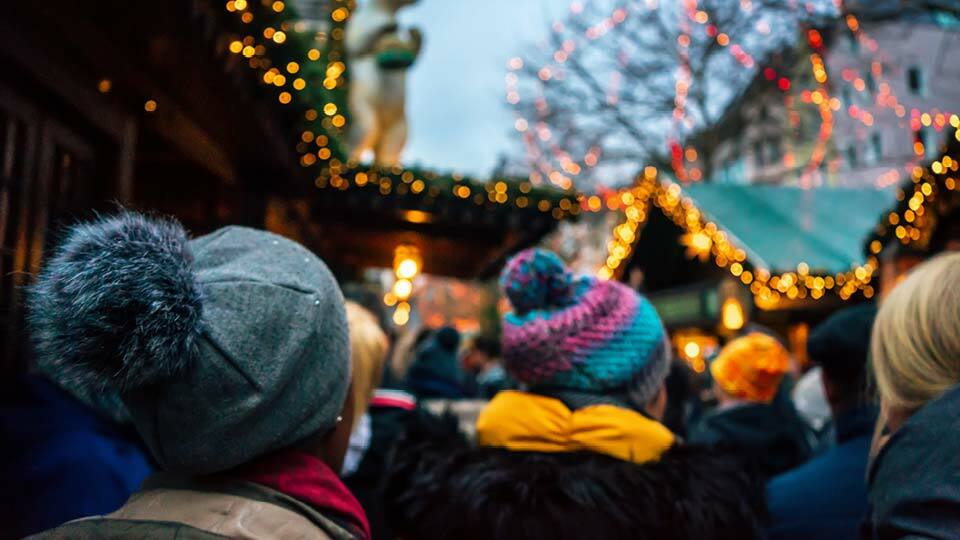 People wearing winter hats walking through a decorated holiday market.