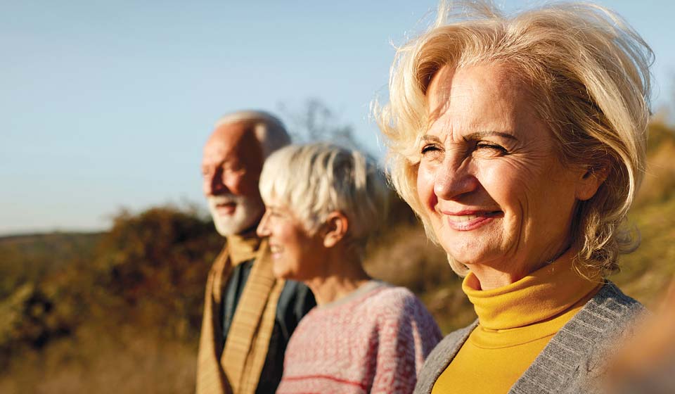 Three older adults smiling while spending time outdoors on a sunny day.