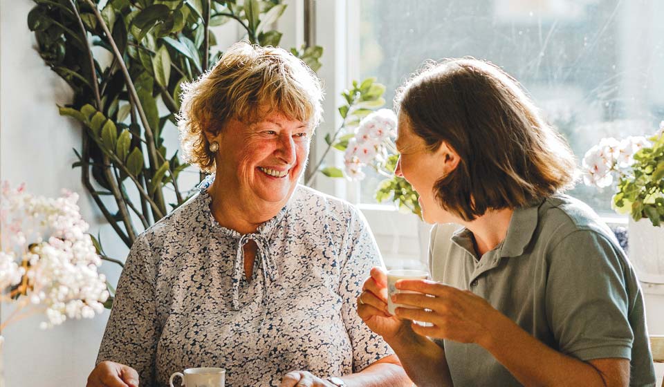 Two women smiling and enjoying a conversation over coffee at home.