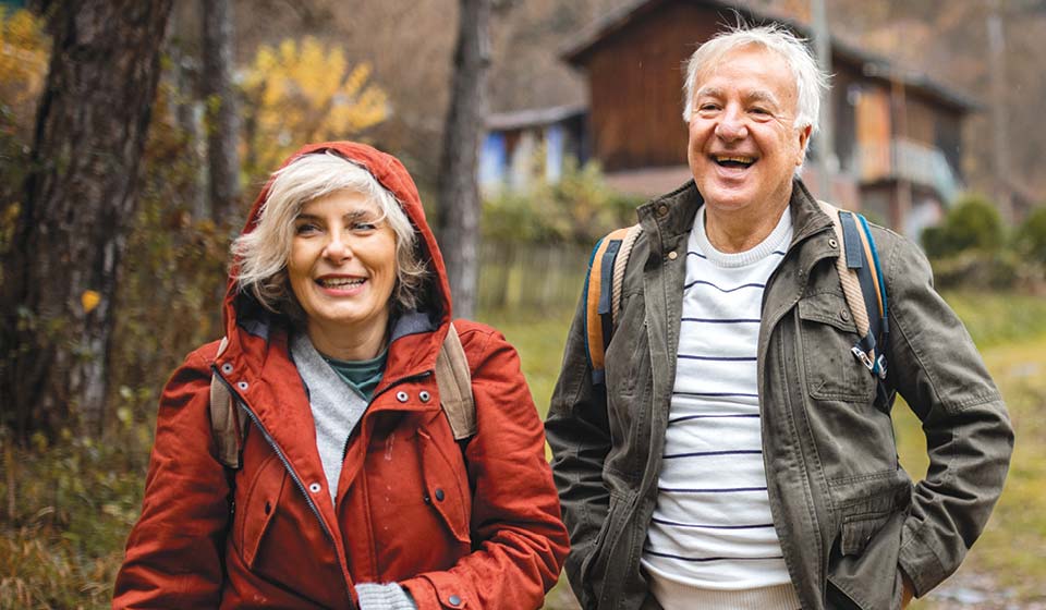 Older couple wearing jackets and backpacks enjoying a walk together outdoors.