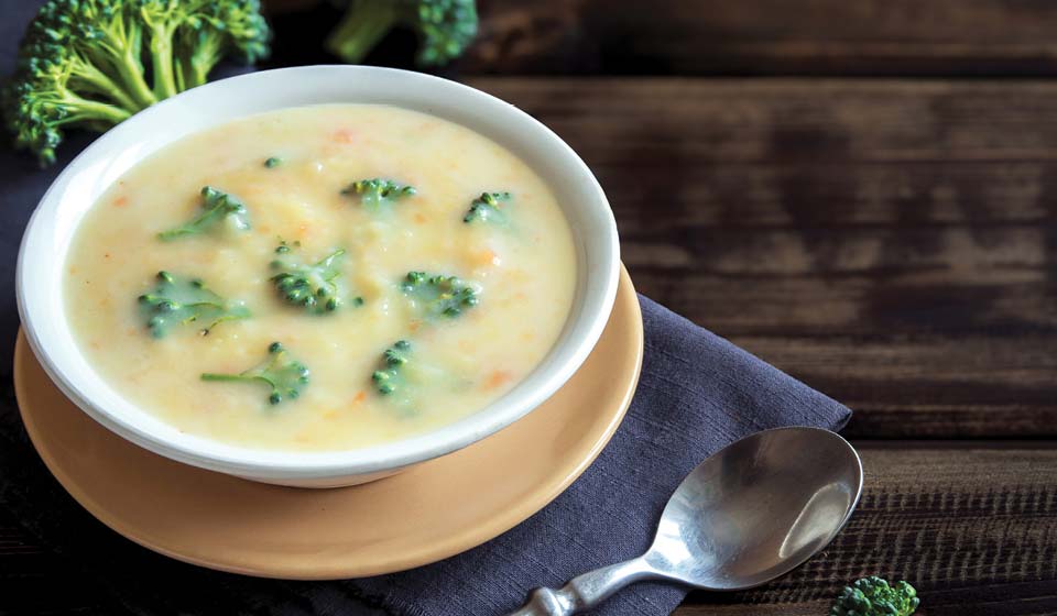 Bowl of creamy broccoli soup served on a wooden table with a spoon beside it.