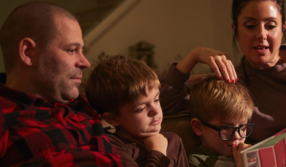 Parents reading a storybook to their two young sons at home.