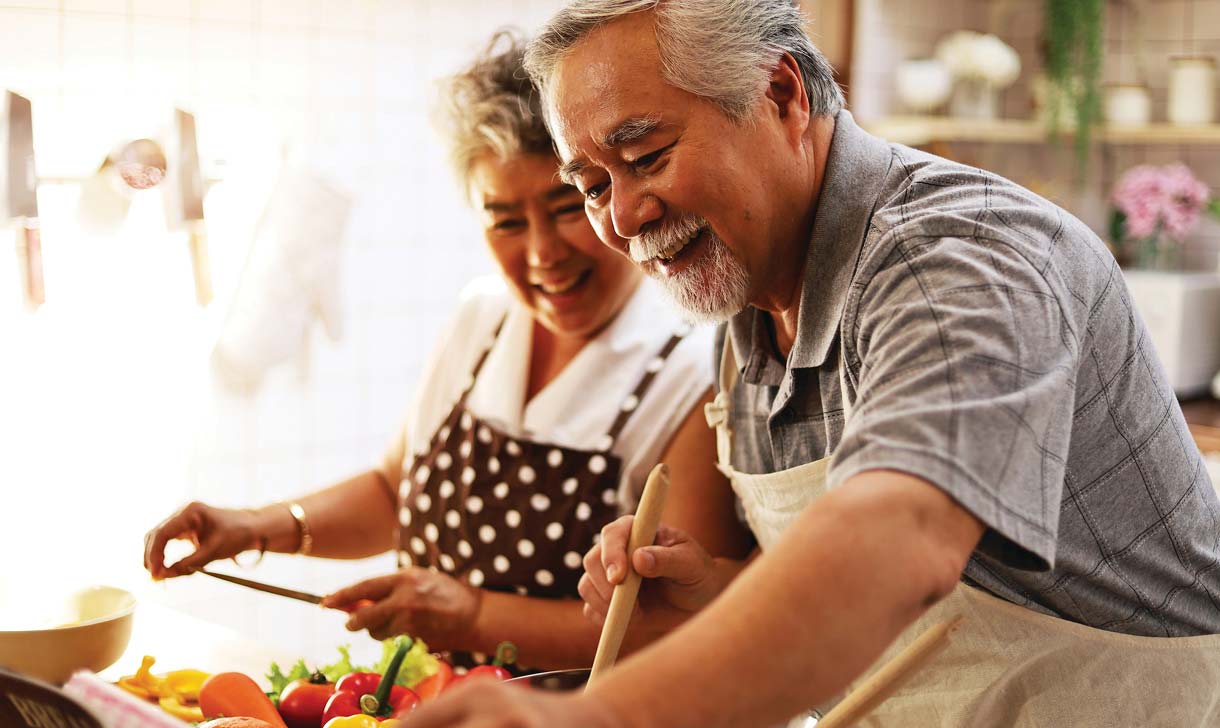 Senior couple smiling while preparing vegetables in the kitchen.
