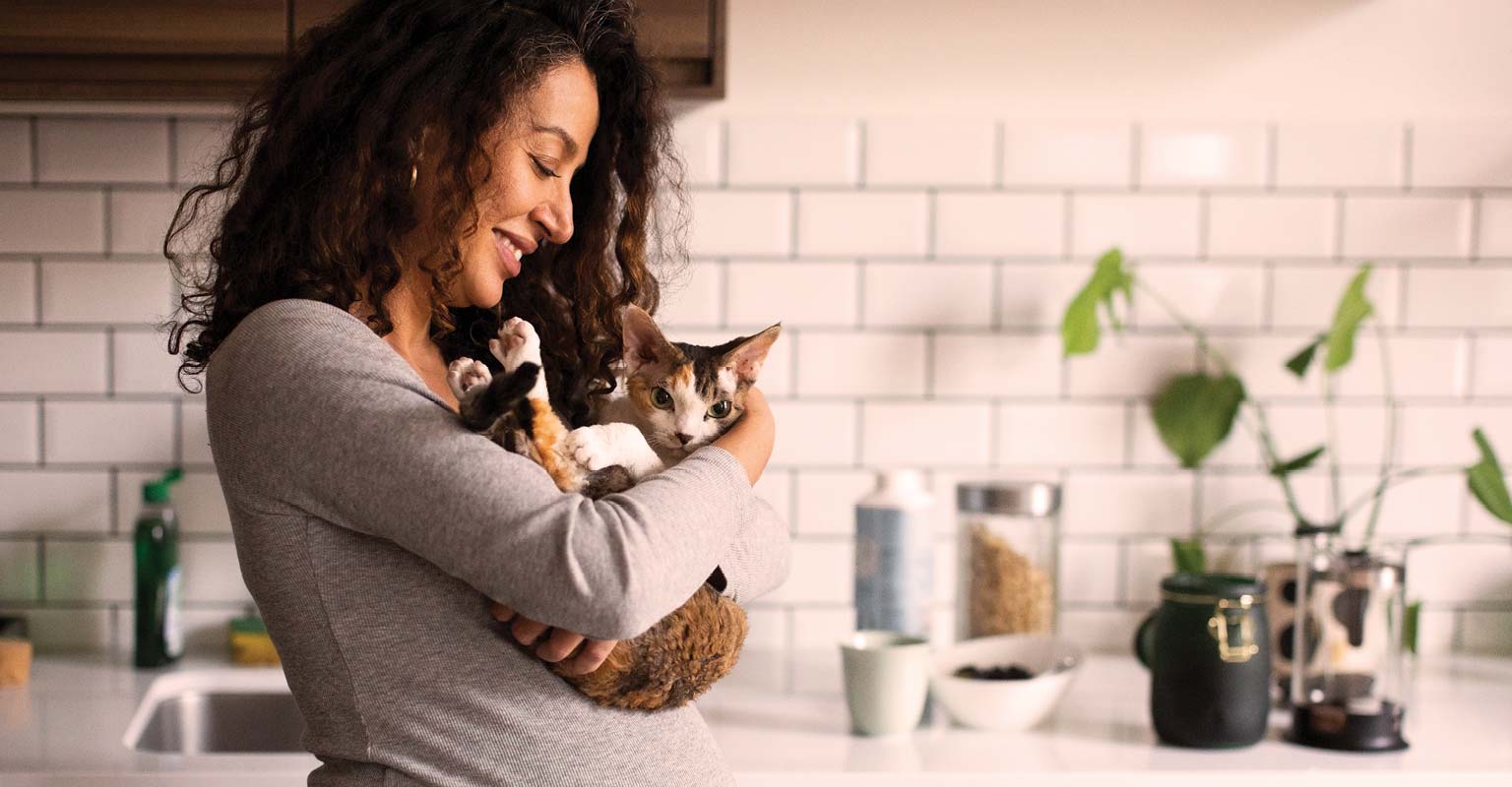 Woman smiling while holding a cat in her kitchen.