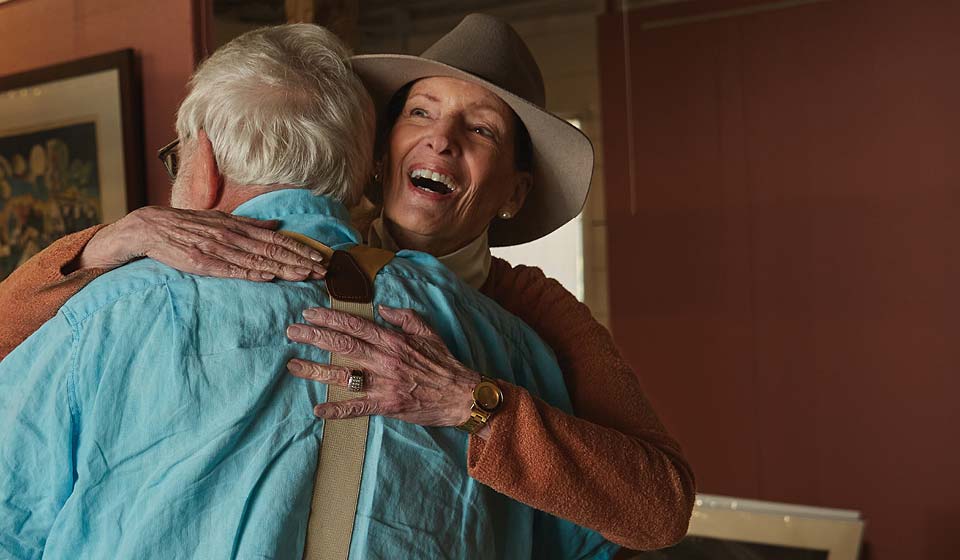 Senior woman hugging a smiling senior man inside a home.