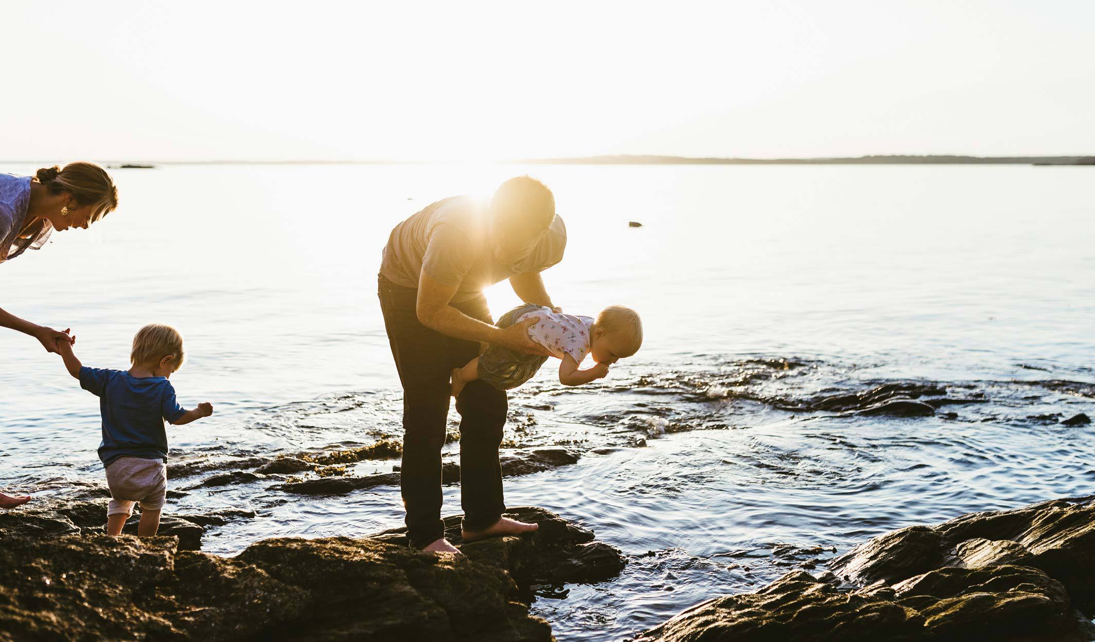 Family playing and exploring near the water’s edge at sunset.