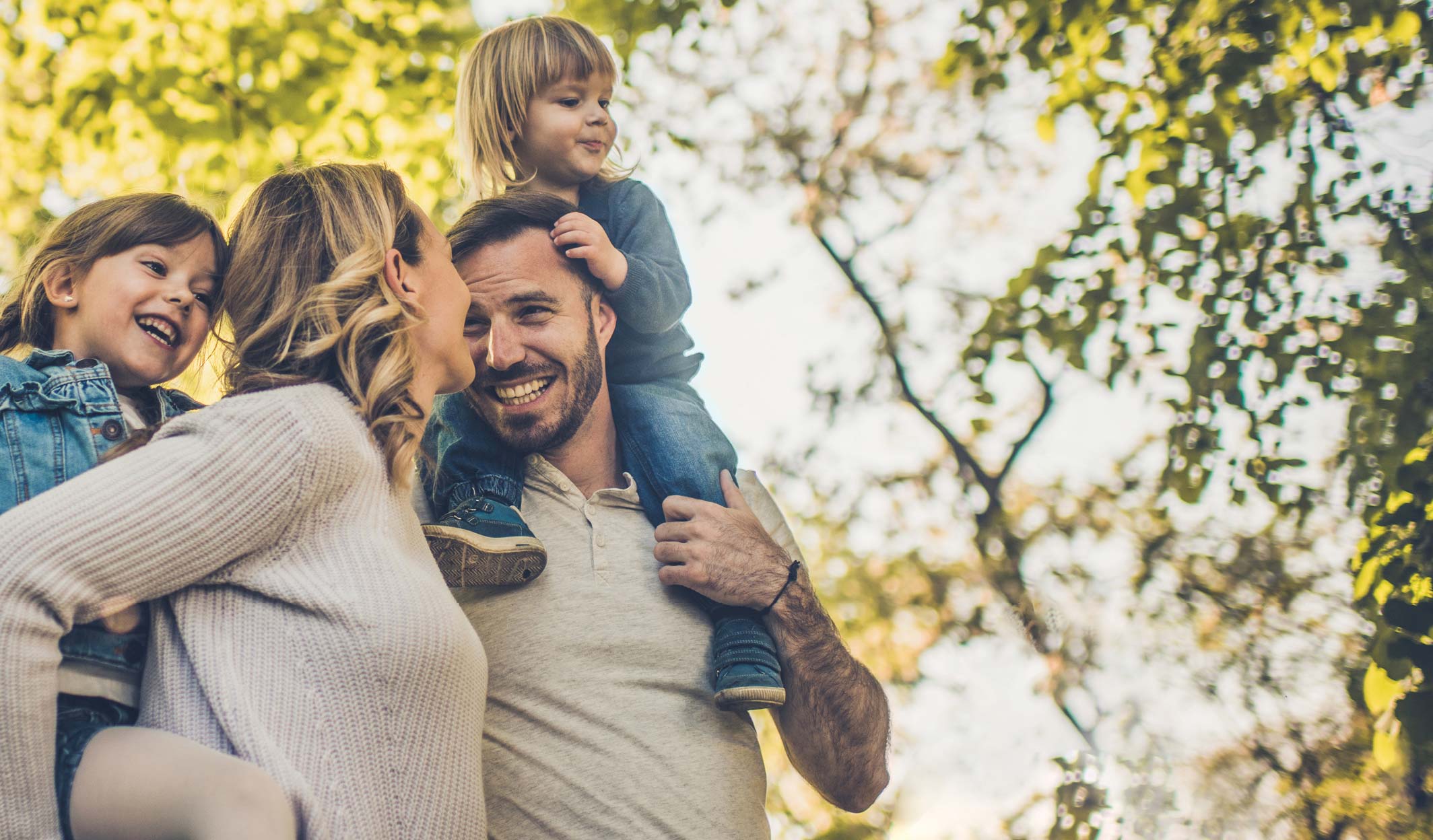 Happy family with two children laughing and walking together in a park.