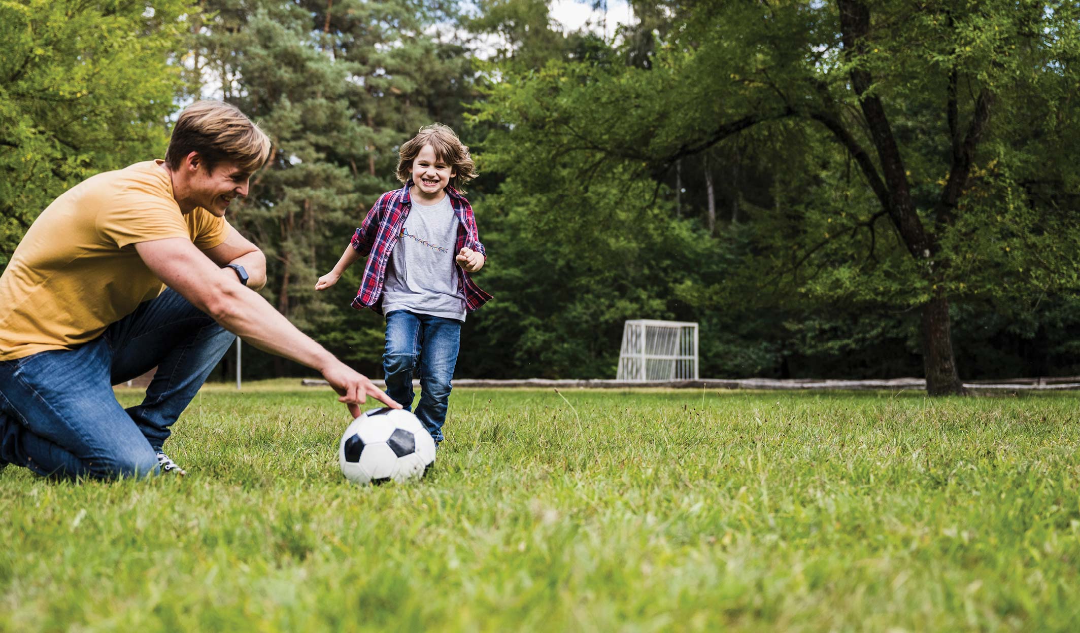 Father playing soccer with his son in a park.