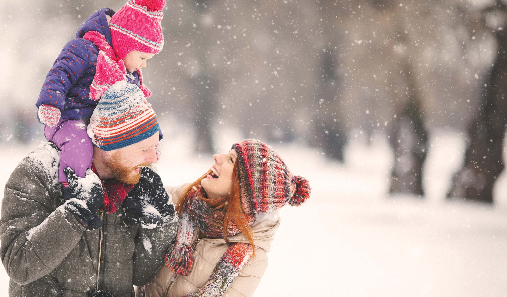 Parent lifting a child in the air while playing in the snow.