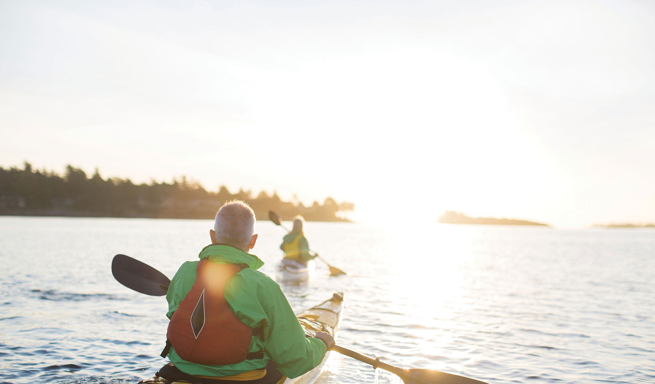 Person kayaking on calm water at sunset.