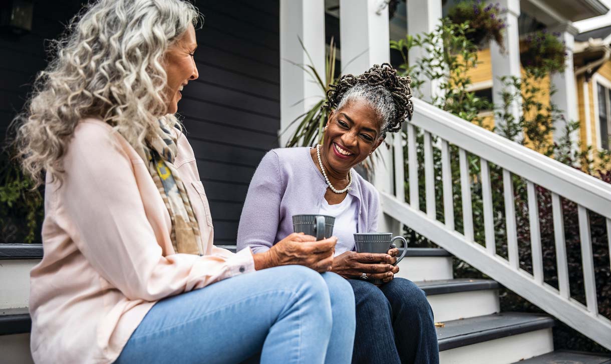 Two women sitting on front steps smiling and looking at a phone together.