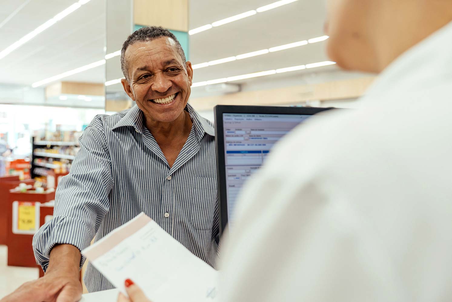 Older man speaking with pharmacy staff at a counter