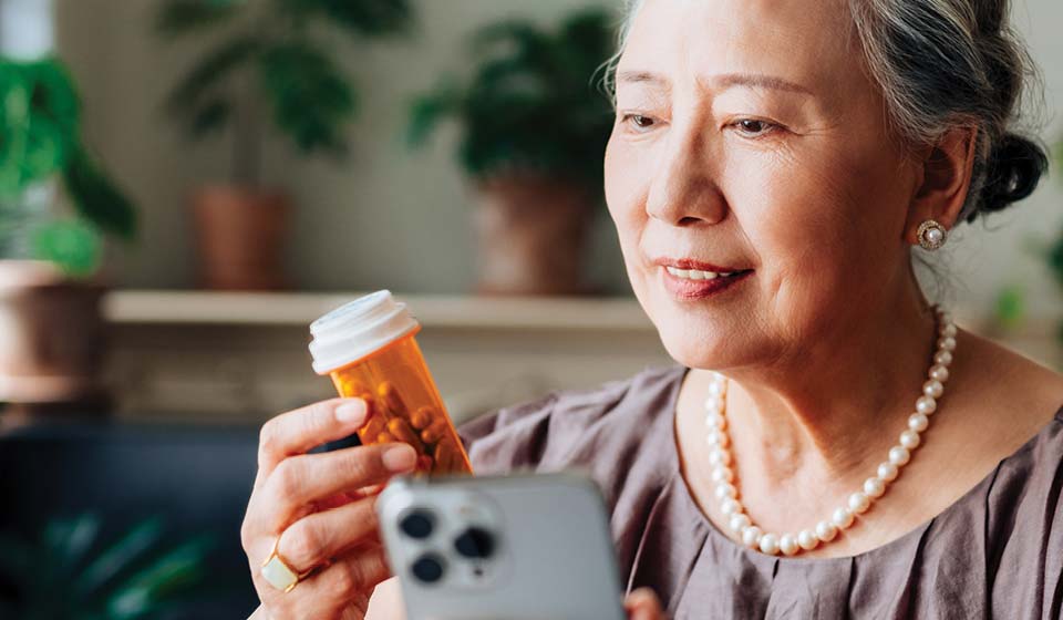 Senior member checking a prescription bottle while using a smartphone.
