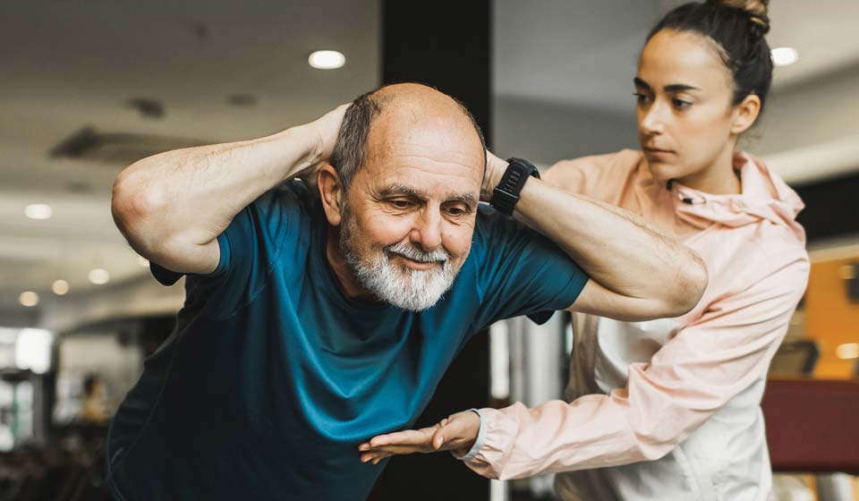 Trainer assisting an older adult with exercise at a fitness center.