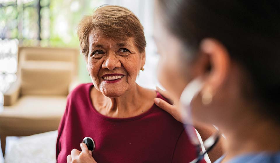 Health care professional assisting a senior member with a home monitoring device.