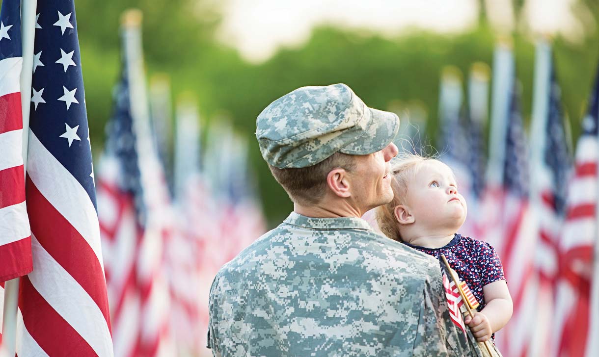 Service member holding a young child with American flags in the background.