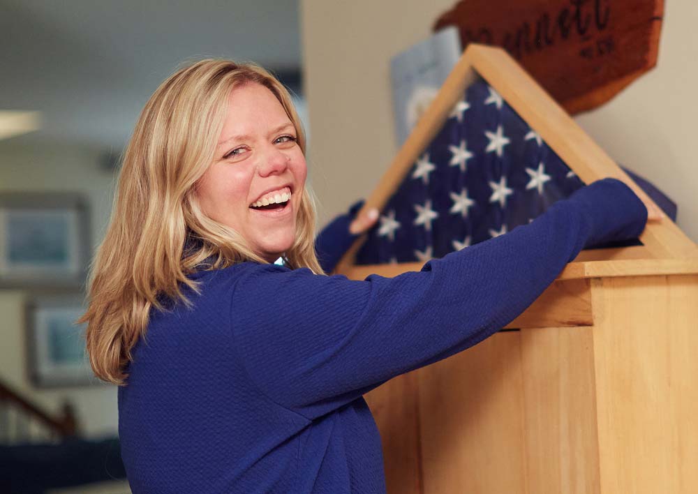 Woman smiling while holding a folded American flag in a wooden case.