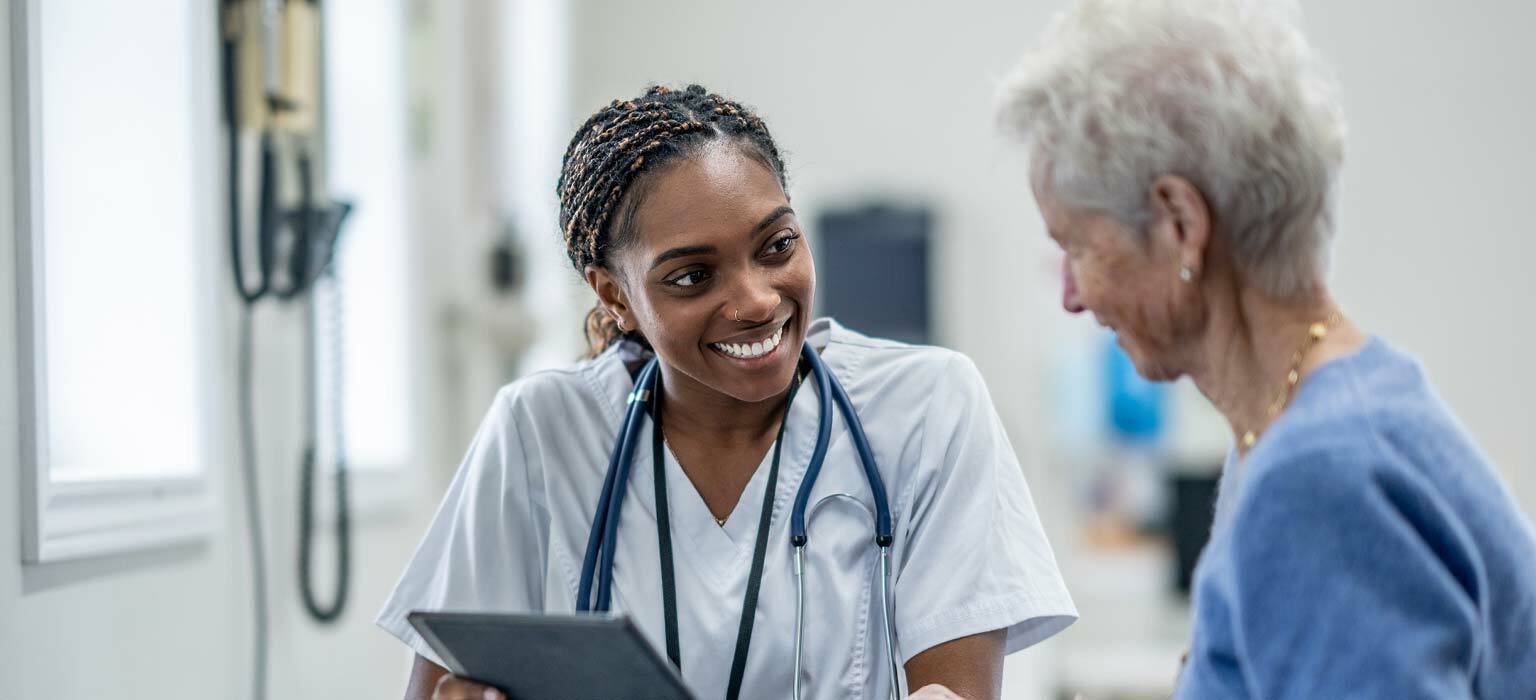 Nurse smiling while showing an elderly patient information on a tablet.