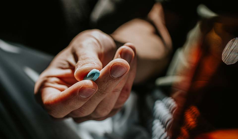 Close-up of a hand holding a small blue pill.