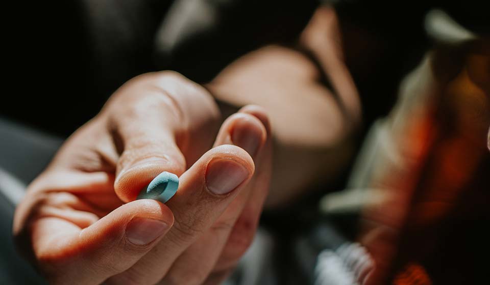 Close-up of a person holding a single pill between their fingers.