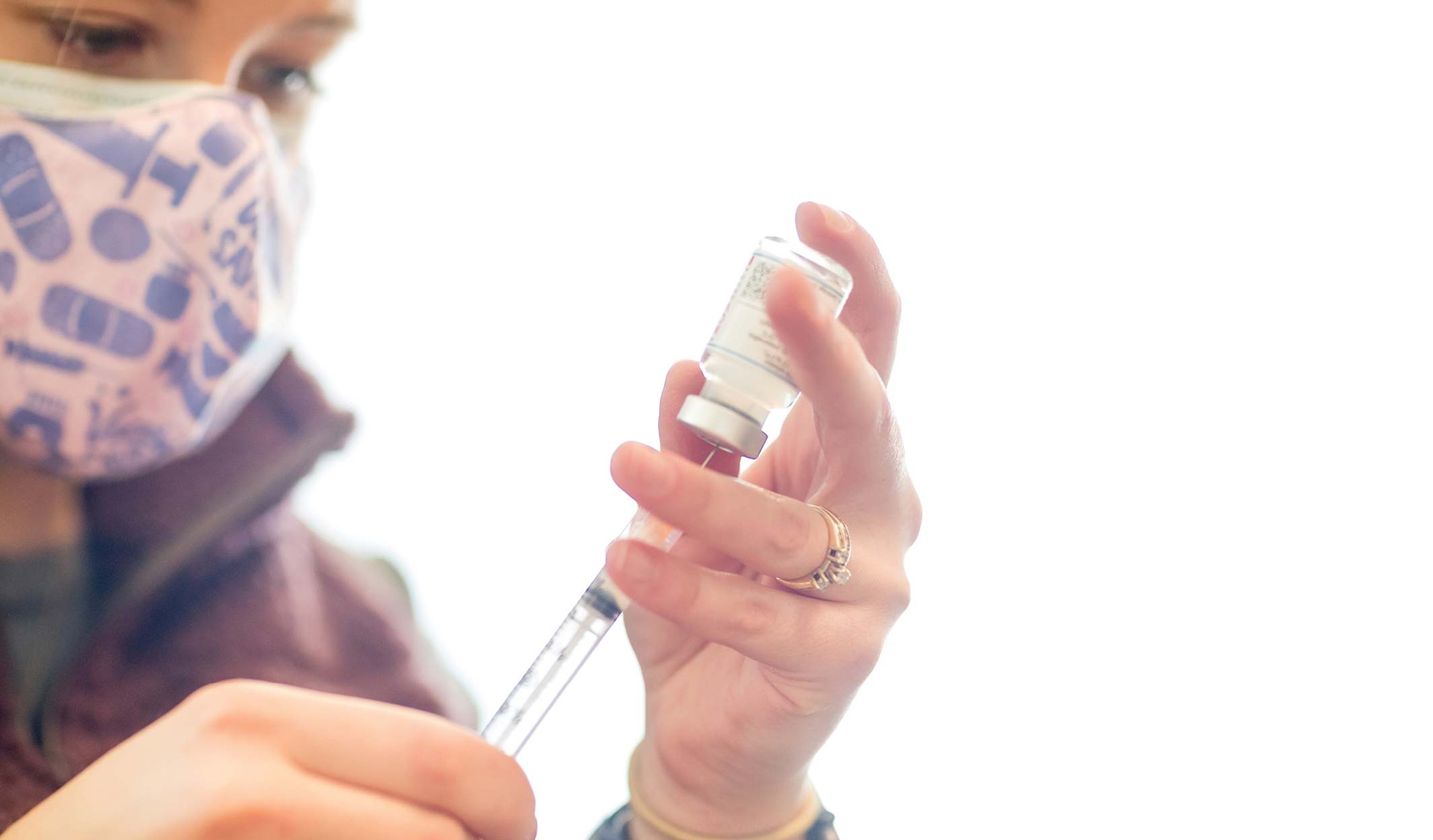 Healthcare worker drawing vaccine into a syringe while wearing a mask.