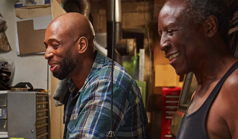 Two men smiling while working together in a workshop.