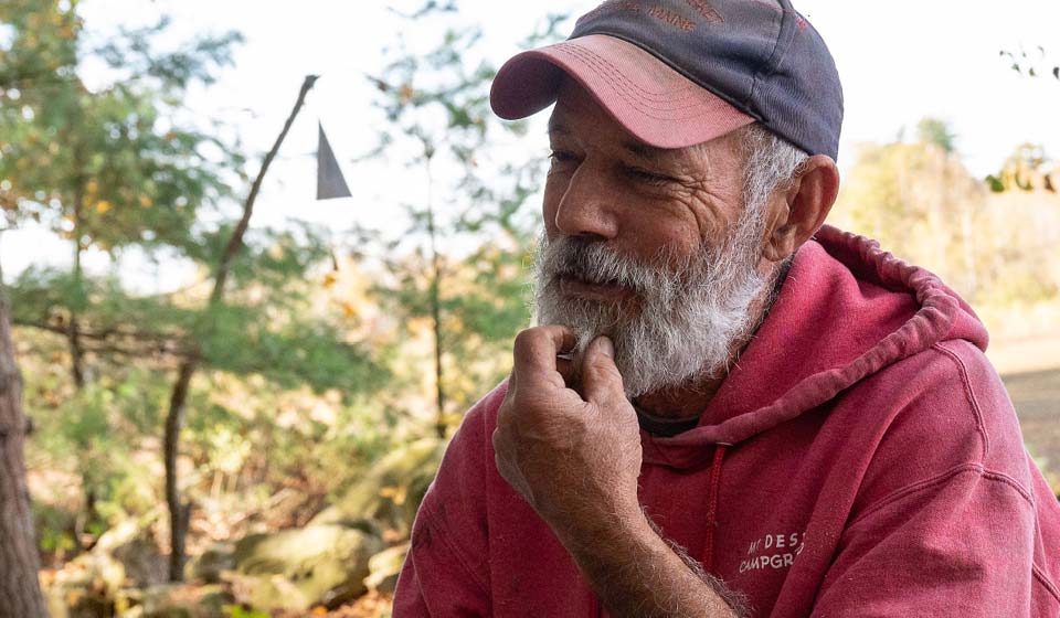 Older man wearing a red sweatshirt and hat, smiling outdoors.